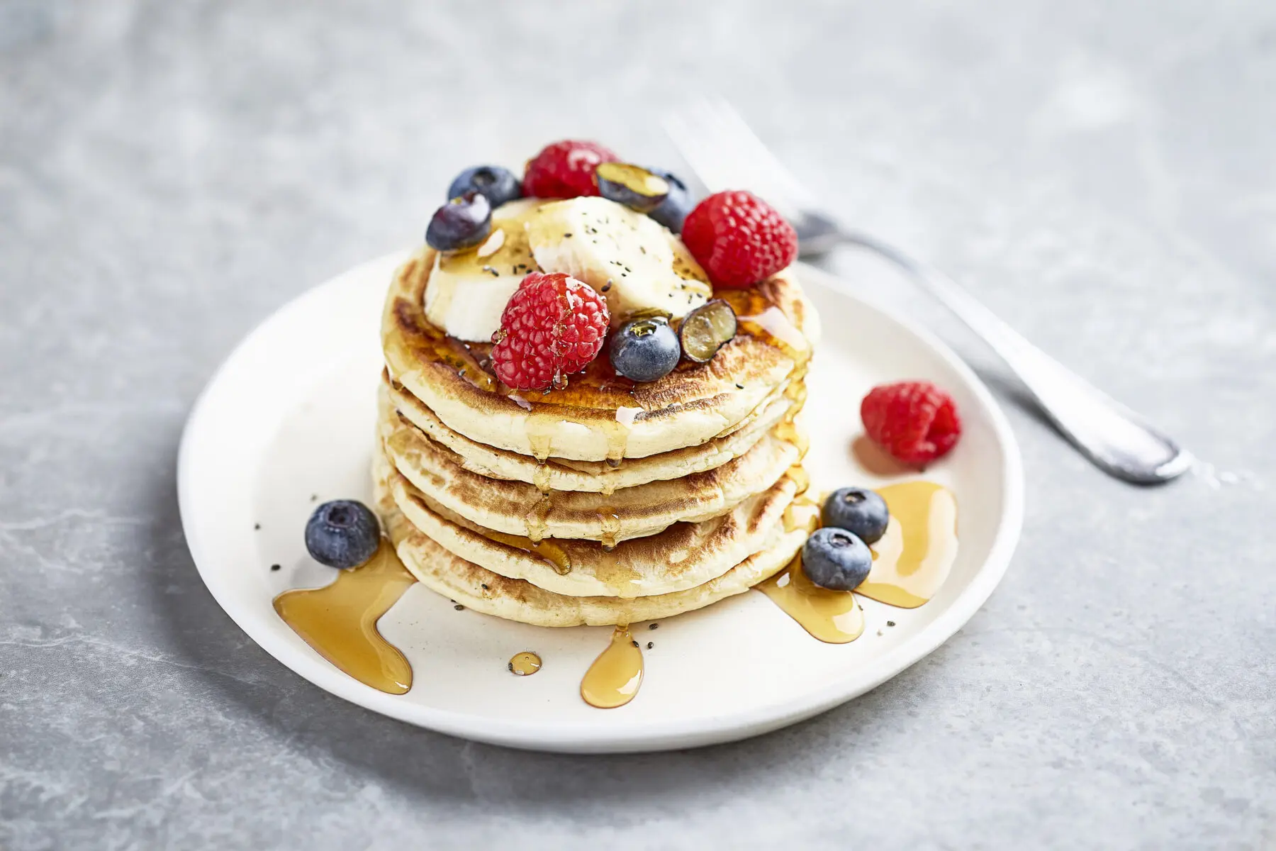 A stack of American Style Pancakes baked using Marriage's Flour dressed with fruit and a drizzle of maple syrup