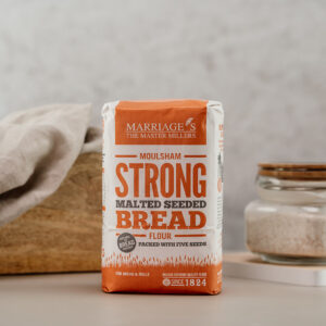 Image of Marriage's Strong Malted Seeded Bread Flour in a white and Orange packet in fron of a loaf of bread on a worksurface.