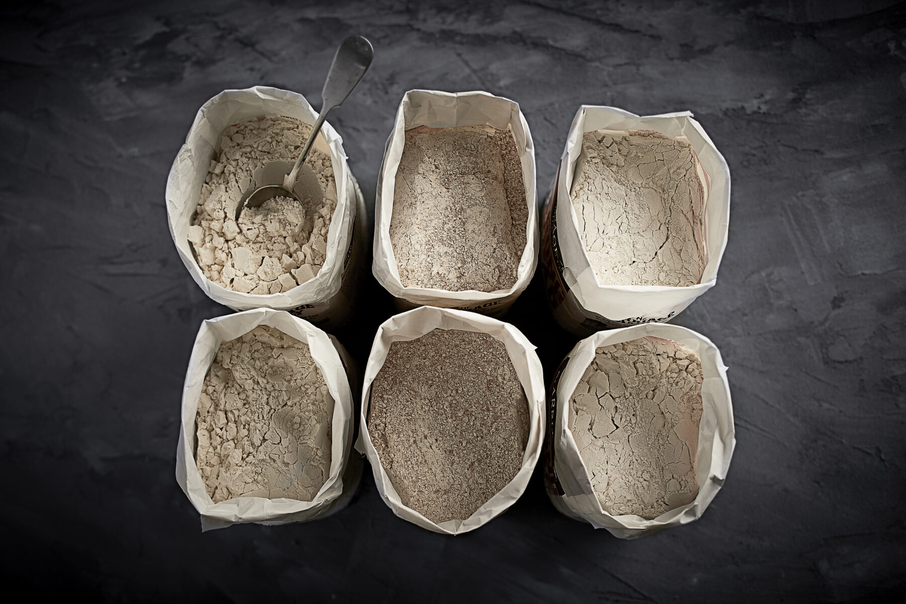 Image taken from above of 6 flour sacks lined up in pairs and filled with white flour